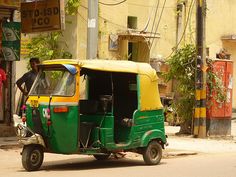 a small green and yellow tuk - tuk parked on the side of a street