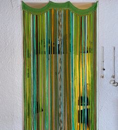 a green curtain hanging on the side of a white wall next to a window with yellow curtains