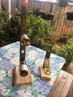 two bottles of wine are sitting on wooden stands in the middle of a table outside