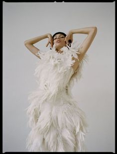 a woman in a white feather dress with her hands on her head and arms behind her head