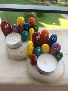 several candles with different colored rocks and faces on them sitting on a window sill