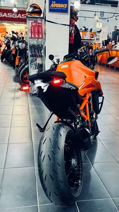 an orange and black motorcycle parked in a showroom with people looking at the motorcycles