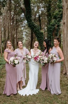 a group of women standing next to each other holding bouquets in front of trees