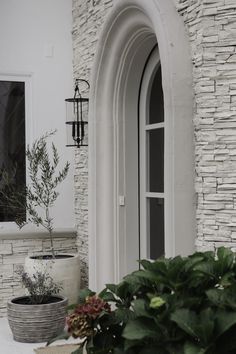 a white house with potted plants in front of the door and an arched window