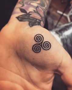 a person with a tattoo on their arm holding up the wrist and hand, which has three spirals tattooed on it