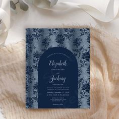 a blue and white wedding card on top of a blanket next to some flowers with ribbons