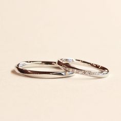 two white gold wedding bands with diamonds on them, set against a plain beige background