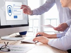 two people working on a computer with a padlock on the screen and paper in front of them