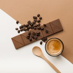 a cup of coffee next to a spoon and chocolate bar on top of a table