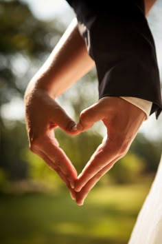 the bride and groom are making a heart shape with their hands as they hold each other