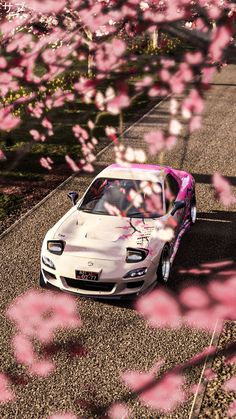 a white car with pink paint on it driving down a road surrounded by trees and flowers