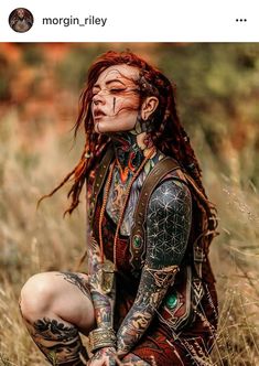 a woman with red hair and tattoos sitting in tall grass