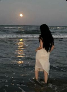 a woman standing in the ocean at sunset