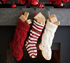 two knitted stockings hanging from a mantel with red and white decorations on it