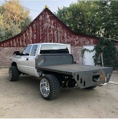 a silver truck parked in front of a red barn with a large metal bed on it's flatbed