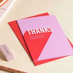 a pink and red thank card sitting on top of a desk next to a pen