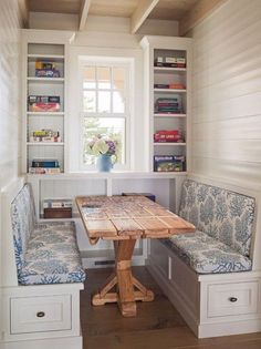 a wooden table sitting under a window next to two blue benches in front of a bookshelf