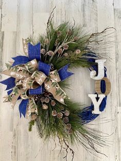 a wreath with the word joy on it and pine cones is hanging on a wooden wall