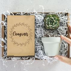 someone is holding a cup in their hand next to a box with congratulations written on it