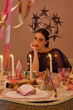 a woman sitting at a table with candles in front of her and stars above her head