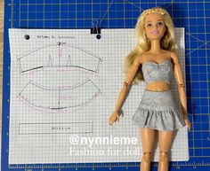 a barbie doll is standing next to a paper cutting mat with measurements for her dress