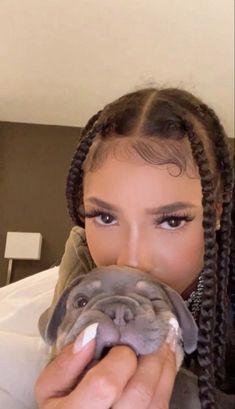 a woman with braids holding a dog in her hand and looking at the camera