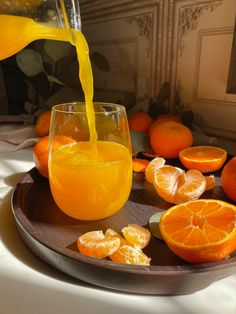 orange juice being poured into a glass on top of a plate with sliced oranges