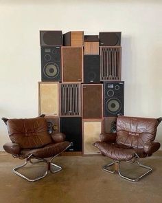 two brown leather chairs sitting next to each other in front of a wall with speakers on it