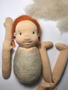 a doll with red hair and green eyes sitting on top of a white surface next to a pair of scissors