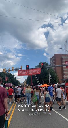 a group of people walking down the street in front of a red sign that says north carolina state university