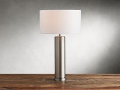 a lamp that is sitting on top of a wooden table in front of a gray wall