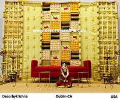 a woman sitting on a red couch in front of a wall with yellow and white decorations