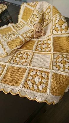 a teddy bear sitting on top of a crocheted blanket with yellow and white squares