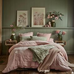 a bedroom with green walls and pink linens on the bed, along with two vases filled with flowers