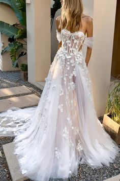 a woman wearing a white wedding dress with flowers on the skirt and off the shoulder