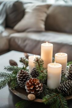 candles and pine cones are arranged on a tray in front of a couch with pillows