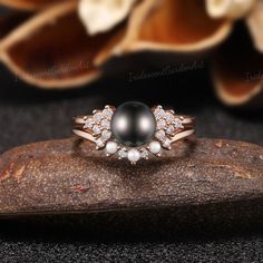 a black pearl and diamond ring sitting on top of a piece of wood with flowers in the background