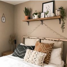 a white bed topped with lots of pillows next to a shelf filled with potted plants