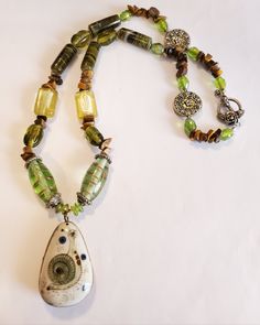 "This is an exquisite necklace made from great quality gemstones and green glass  The tubular green swirl agate gemstone measures 1\" long, 3/8\" wide. The swirl design appears brown, green and black swirl design. There are 4 in the design pattern of necklace There are 2 square shape clear light yellow beads, measures 3/8\" long, 1/2\" wide, with a touch of ivory color on the inside In the pattern there are swarvoski clear light green beads to accent the, Tiger Eye chips are in the pattern desig Green Jade Beaded Necklaces, Green Teardrop Czech Glass Jewelry, Green Czech Glass Teardrop Jewelry, Unique Green Natural Stone Necklace, Green Natural Stone Teardrop Pendant Necklace, Green Beaded Teardrop Pendant Jewelry, Unique Green Agate Necklaces, Artisan Green Pendant Necklace, Green Artisan Pendant Necklace