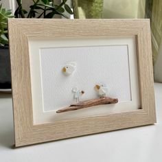 two little birds sitting on a branch in front of a white framed photo with wood frame