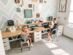 two young children sitting at a desk in front of a wall with chevron patterns