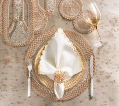 a place setting with gold and white plates, napkins, silverware and wine glasses