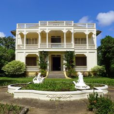 a white building with statues in front of it and bushes around the entrance area, on a sunny day