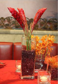 two vases filled with flowers on top of a red table cloth covered tablecloth