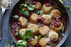 a pan filled with meatballs covered in sauce and garnished with basil leaves