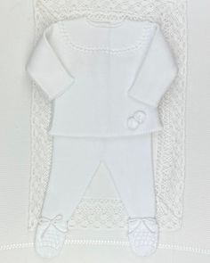 a white knitted baby outfit and booties laying on top of a lace doily