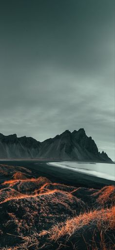 an orange and black landscape with mountains in the backgrounnd, on a cloudy day