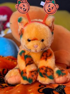 a small stuffed animal with orange and green designs on it's ears sitting on an orange blanket