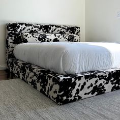 a black and white cow print bed in a room with carpeted flooring next to a wall