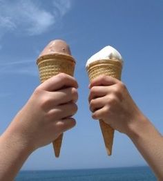 two hands holding ice cream cones against a blue sky